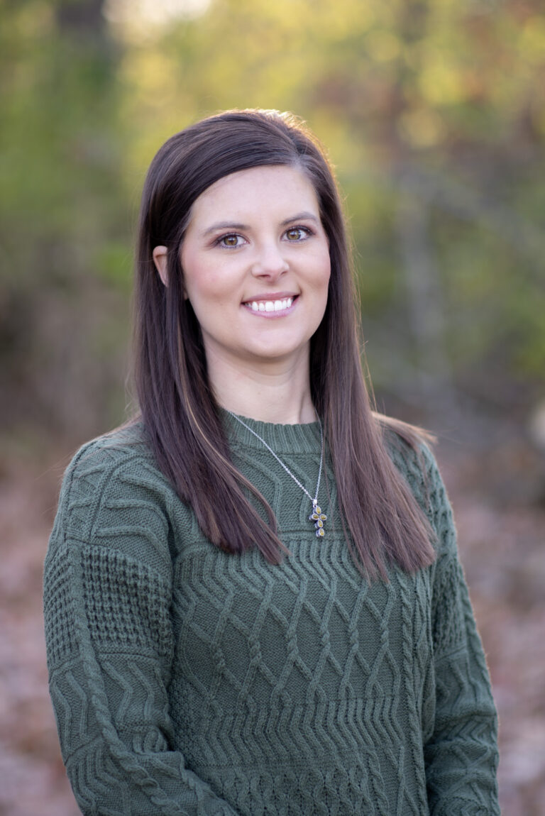 Ashley Reed, team member at Duckett Ladd Advisors, smiling outdoors in a green sweater, with a blurred natural background.